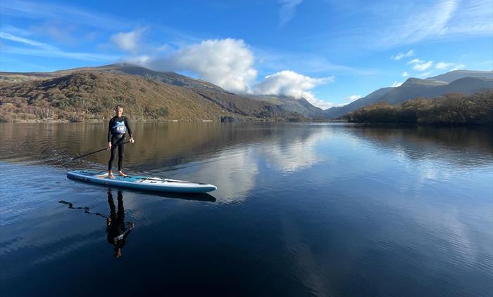 Picture of a man on a paddleboard with flat water and mountains in the background.